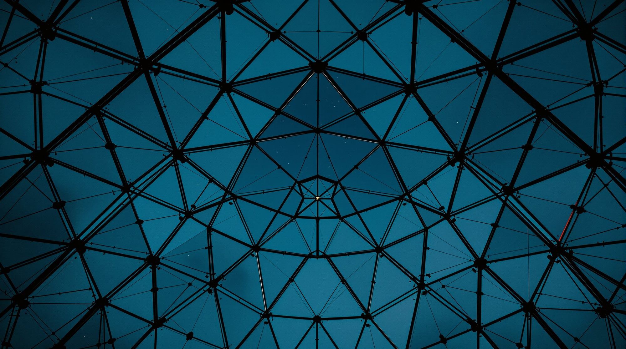 A geodesic dome's struts traced against a dusk sky, the low sun flaring through the triangles
